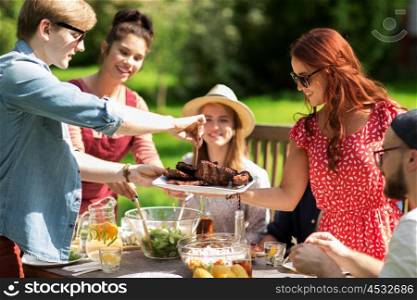 leisure, holidays, eating, people and food concept - happy friends having meat for dinner at summer garden party
