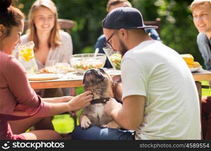 leisure, holidays, eating, people and food concept - happy friends with french bulldog dog having dinner at summer garden party
