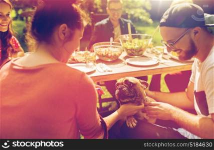 leisure, holidays, eating, people and food concept - happy friends with french bulldog dog having dinner at summer garden party. happy friends having dinner at summer garden party