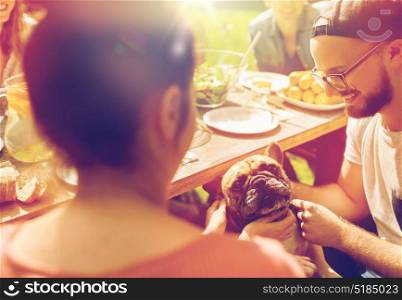 leisure, holidays, eating, people and food concept - happy friends with french bulldog dog having dinner at summer garden party. happy friends having dinner at summer garden party
