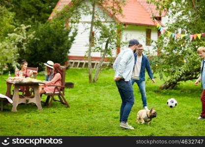 leisure, holidays, people and pets concept - happy friends playing football with dog at summer garden party