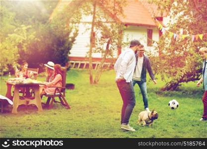 leisure, holidays, people and pets concept - happy friends playing football with dog at summer garden party. friends playing football with dog at summer garden