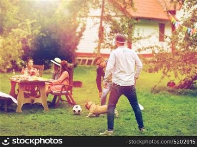 leisure, holidays, people and pets concept - happy friends playing football with dog at summer garden party. friends playing football with dog at summer garden