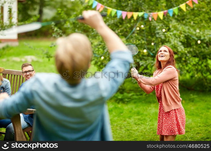 leisure, holidays, people and sport concept - happy friends playing badminton or shuttlecock at summer garden party
