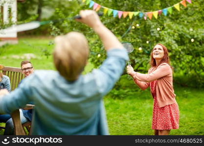 leisure, holidays, people and sport concept - happy friends playing badminton or shuttlecock at summer garden party