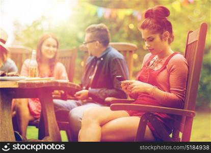 leisure, holidays, people and technology concept - young woman or teenage girl texting on smartphone and friends having dinner at summer garden party. woman with smartphone and friends at summer party