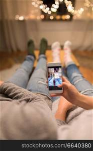leisure, hygge and christmas concept - close up of couple taking foot selfie by smartphone and garland lights at home. close up of couple taking foot photo by smartphone