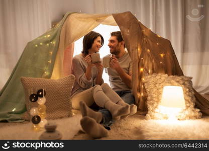 leisure, hygge and people concept - happy couple drinking coffee or tea in kids tent at home. couple drinking coffee or tea in kids tent at home