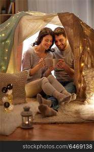 leisure, hygge and people concept - happy couple drinking coffee or tea in kids tent at home. couple drinking coffee or tea in kids tent at home