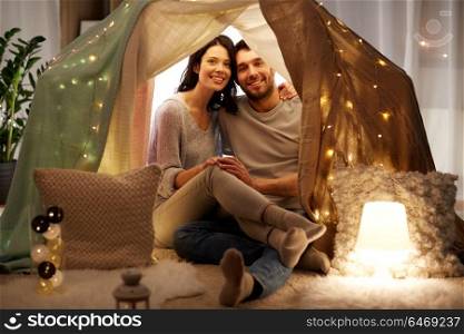 leisure, hygge and people concept - happy couple in kids tent at home. happy couple in kids tent at home