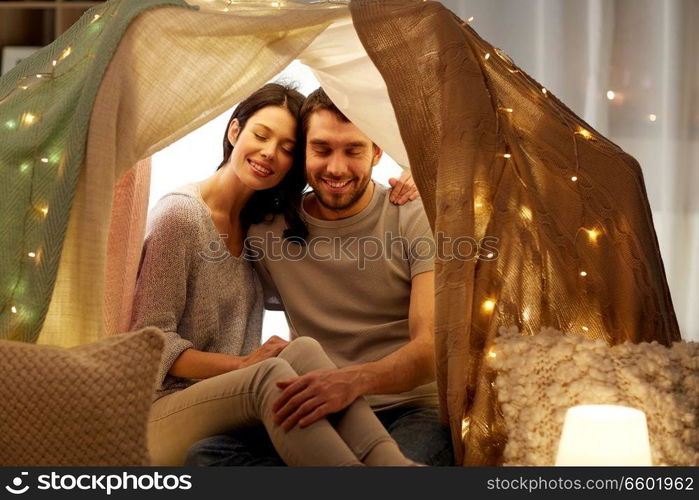 leisure, hygge and people concept - happy couple in kids tent at home. happy couple in kids tent at home