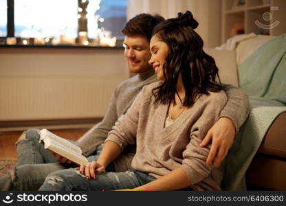 leisure, hygge and people concept - happy couple reading book at home. happy couple reading book at home