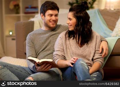 leisure, hygge and people concept - happy couple reading book at home. happy couple reading book at home