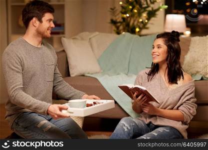 leisure, hygge and people concept - happy couple with book and food on tray at home. happy couple with book and food at home
