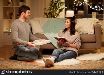 leisure, hygge and people concept - happy couple with book and food on tray at home. happy couple with book and food at home