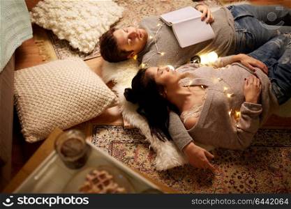 leisure, hygge and people concept - happy couple with book and garland lying on floor at home and sleeping. happy couple with garland lying on floor at home