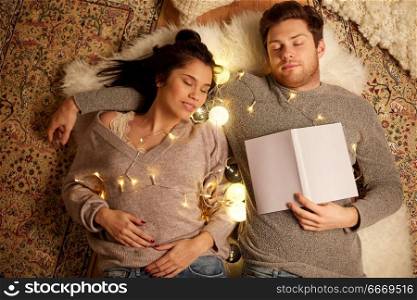 leisure, hygge and people concept - happy couple with book and garland lying on floor at home and sleeping. happy couple with garland lying on floor at home. happy couple with garland lying on floor at home