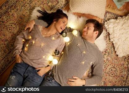 leisure, hygge and people concept - happy couple with garland at home. happy couple with garland lying on floor at home