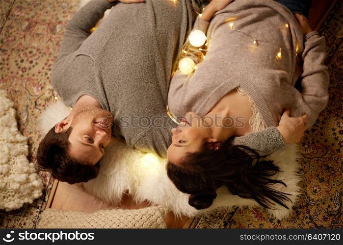 leisure, hygge and people concept - happy couple with garland at home. happy couple with garland lying on floor at home