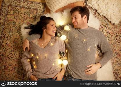 leisure, hygge and people concept - happy couple with garland at home. happy couple with garland lying on floor at home. happy couple with garland lying on floor at home