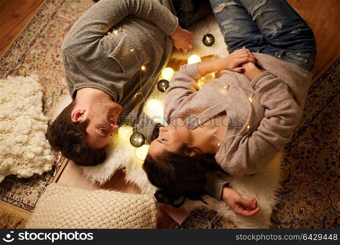 leisure, hygge and people concept - happy couple with garland lying on floor at home. happy couple with garland lying on floor at home