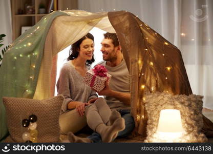 leisure, hygge and people concept - happy couple with gift box in kids tent at home. happy couple with gift box in kids tent at home