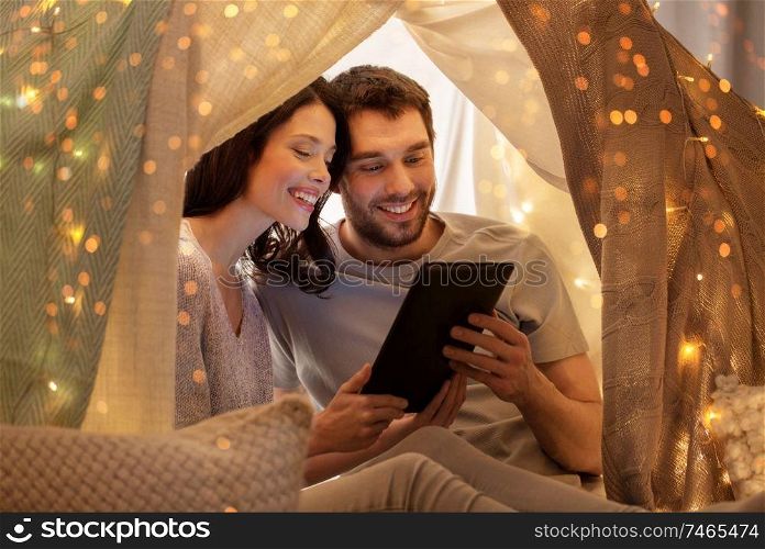 leisure, hygge, technology and people concept - happy couple with tablet pc computer in kids tent at home. happy couple with tablet pc in kids tent at home