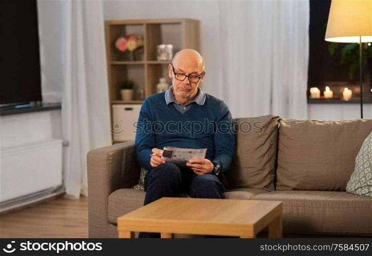 leisure, information and old people concept - bald senior man in glasses solving crossword puzzle at home in evening. senior man in glasses solving crossword at home