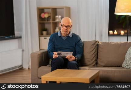 leisure, information and old people concept - bald senior man in glasses solving crossword puzzle at home in evening. senior man in glasses solving crossword at home