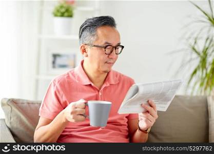 leisure, information, people and mass media concept - happy man in glasses reading newspaper and drinking coffee at home. man drinking coffee and reading newspaper at home
