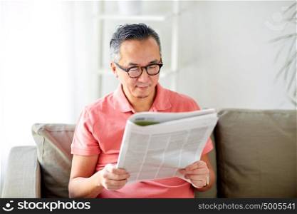 leisure, information, people and mass media concept - happy man in glasses reading newspaper at home. happy man in glasses reading newspaper at home