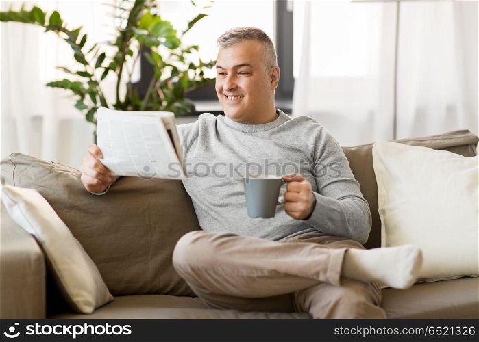 leisure, information, people and mass media concept - man reading newspaper and drinking coffee at home. man reading newspaper and drinking coffee at home