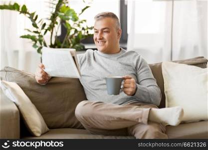 leisure, information, people and mass media concept - man reading newspaper and drinking coffee at home. man reading newspaper and drinking coffee at home
