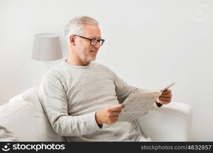 leisure, information, people and mass media concept - senior man in glasses reading newspaper at home