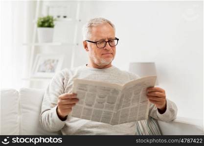 leisure, information, people and mass media concept - senior man in glasses reading newspaper at home