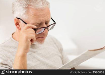 leisure, information, people, vision and mass media concept - close up of senior man in glasses reading newspaper at home