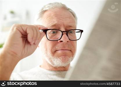 leisure, information, people, vision and mass media concept - close up of senior man in glasses reading newspaper at home