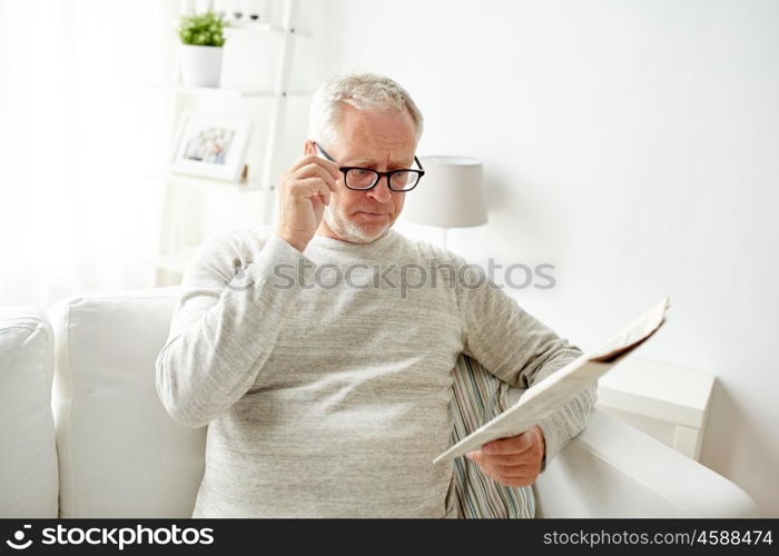 leisure, information, people, vision and mass media concept - senior man in glasses reading newspaper at home