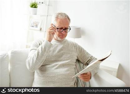 leisure, information, people, vision and mass media concept - senior man in glasses reading newspaper at home