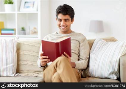 leisure, literature and people concept - happy man sitting on sofa and reading book at home. man sitting on sofa and reading book at home
