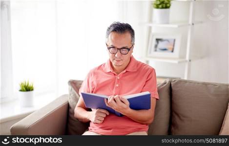 leisure, literature and people concept - man sitting on sofa and reading book at home. man sitting on sofa and reading book at home