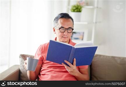 leisure, literature and people concept - man sitting on sofa with mug and reading book at home. man sitting on sofa and reading book at home