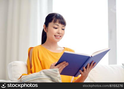 leisure, literature and people concept - smiling young asian woman reading book at home