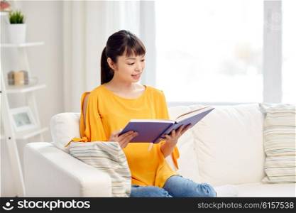 leisure, literature and people concept - smiling young asian woman reading book at home