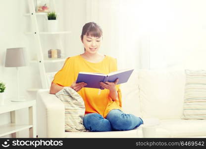 leisure, literature and people concept - smiling young asian woman reading book at home. smiling young asian woman reading book at home