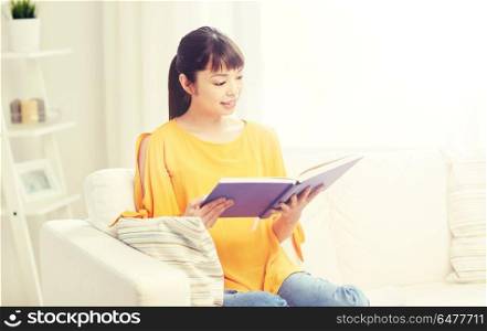 leisure, literature and people concept - smiling young asian woman reading book at home. smiling young asian woman reading book at home. smiling young asian woman reading book at home