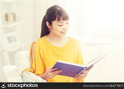 leisure, literature and people concept - smiling young asian woman reading book at home. smiling young asian woman reading book at home. smiling young asian woman reading book at home