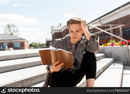 leisure, literature and people concept - young man or teenage boy reading book or diary in city. young man or teenage boy reading book in city