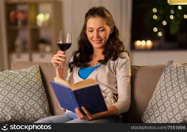 leisure, literature and people concept - young woman reading book and drinking red wine at home in evening. young woman reading book and drinking wine at home