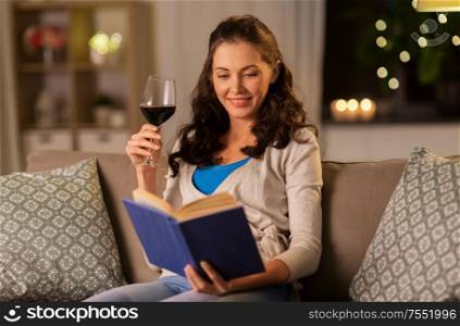 leisure, literature and people concept - young woman reading book and drinking red wine at home in evening. young woman reading book and drinking wine at home
